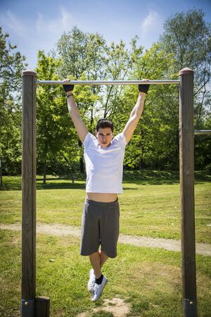Attractive young man exercising and working out in outdoor gym in city park