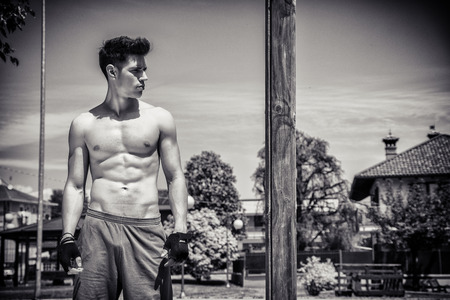 Attractive shirtless young man resting after workout in outdoor gym in city park. Black and white shotの写真素材