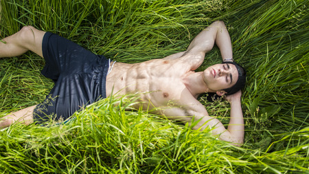 Attractive, fit muscular shirtless young man relaxing lying in a field in the countryside, with eyes closedの写真素材