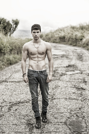 Shirtless sexy muscular young man in jeans walking along rural road in filtered, unsaturated photoの写真素材