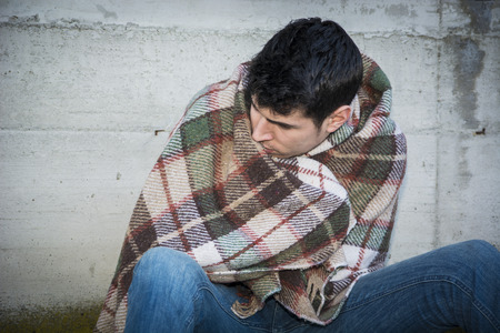 Young male beggar on city sidewalk with blanket on his shouldersの写真素材