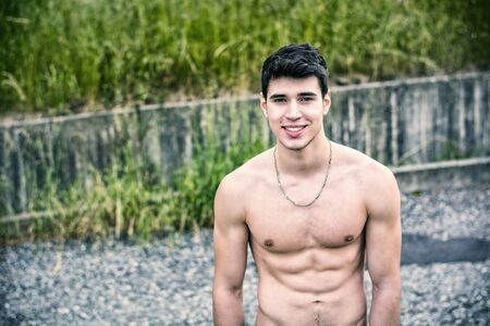 Shirtless sexy muscular young man in jeans walking along rural roadの写真素材