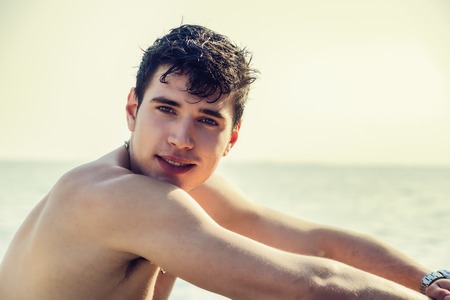 Attractive young man in the sea getting out of water with wet hair, looking in camerの写真素材