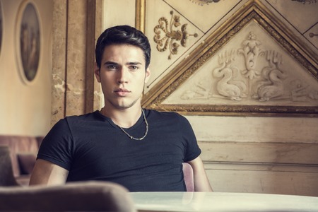 Handsome young man sitting in vintage retro elegant place in Europe, looking at cameraの写真素材