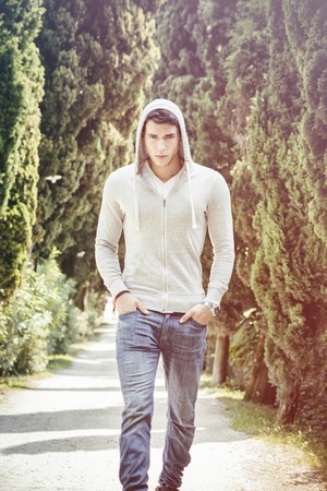 Handsome young man walking along rural road with hoodie, looking confident and relaxedの写真素材