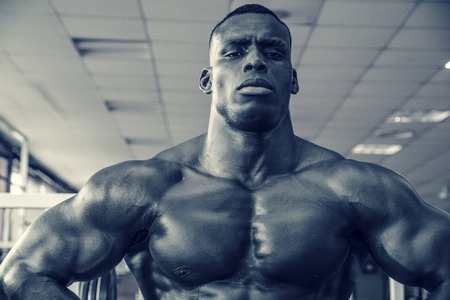 Attractive hunky black male bodybuilder doing bodybuilding pose in gymの写真素材