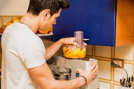 Young man preparing healthy smoothie drink in mixer, made from blended fresh tropical fruit offering a toast or greetingの写真素材