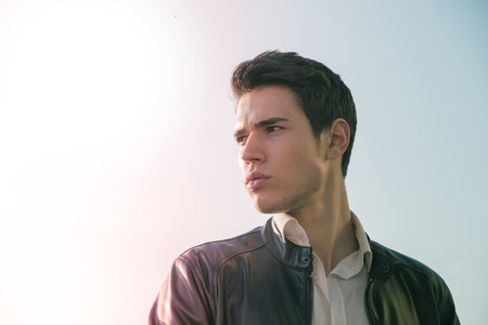Handsome young man at countryside, in front of field or grassland, wearing white shirt and jacket, looking at cameraの写真素材