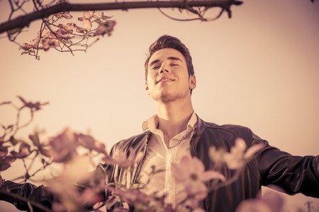 Good looking male model at couuntryside, among flowers, enjoying nature with eyes closedの写真素材
