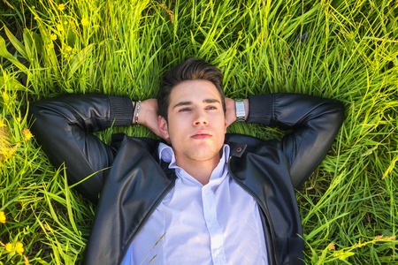Good looking, fit male model relaxing lying on the grass, looking at camera, photographed right from...