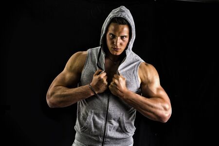Muscular man with blue hoodie on bare chest, isolated on black backgroundの写真素材