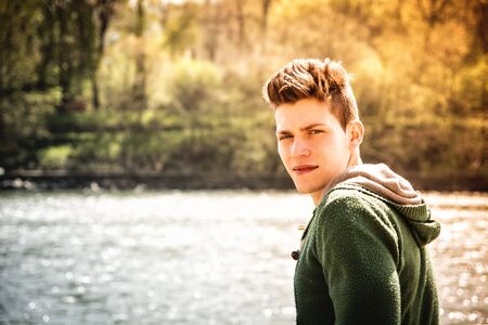 Head and shoulders length of contemplative light brown haired teenage boy wearing green hooded-shirt...
