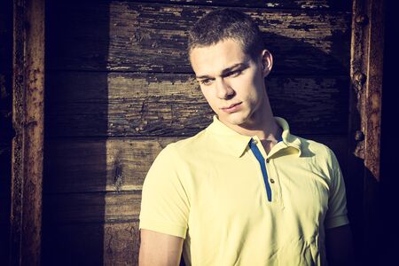 Handsome young man leaning against wood planks wall outdoor and looking downの写真素材