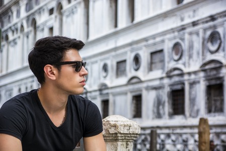 Portrait of Attractive Dark Haired Young Man Leaning Against Railing on Foot Bridge Over Narrow Canal in Venice, Italyの写真素材