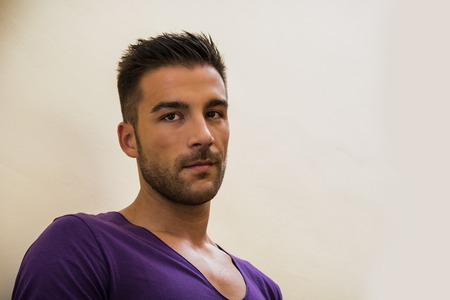 Head and shoulders shot of handsome young man with purple t-shirt, looking at camera, on light backgroundの写真素材