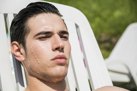 Shirtless Young Man Drying Off in Hot Sun, Muscular Man Wearing Bathing Suit and Sunglasses Sunbathing on Lounge Chair on Grassの写真素材