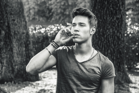 Attractive young man in park next to trees, looking away to a side