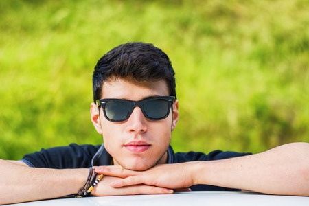 Head and arms shot of handsome attractive young man looking at camera outdoor, leaning on flat surface with head resting on handsの写真素材