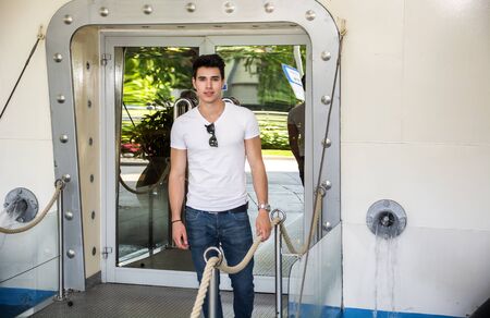Handsome trendy male passenger on a ship, standing on the gangway reflected in the glass door...