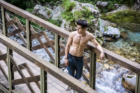 High Angle View of a Shirtless Athletic Man Leaning Against Wooden Pathway Rail at the River.の写真素材