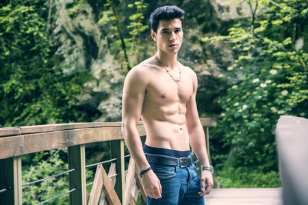 Shirtless Athletic Man Standing on Wooden Bridge on the River in the Woodsの写真素材
