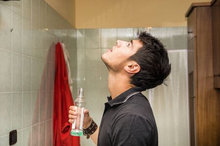 Handsome young man using mouthwash to clean his teeth and mouth, in his home bathroomの写真素材