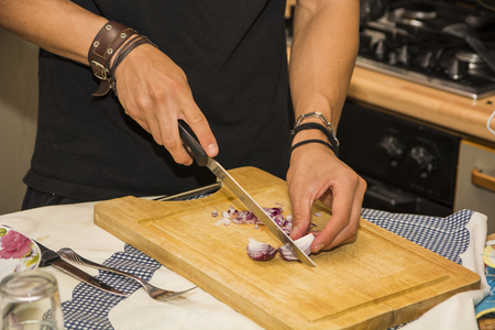 Close up of Young Man's hands Chopping Red Onion with Sharp Knife in Kitchen - Close Up of Man Cooking in Kitchen of First Apartmentの写真素材