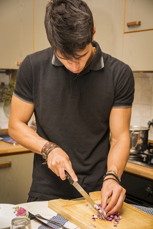 Waist Up of Attractive Young Man with Dark Hair, Chopping Red Onion with Sharp Knife in Kitchen -...