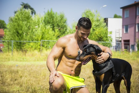 Half Body Shot of a Shirtless Athletic Young Man with his Dog and Looking at Itの写真素材