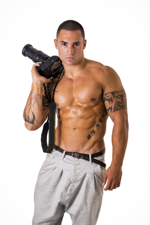 Handsome shirtless athletic young male photographer with professional photo camera in hand, isolated on whiteの写真素材