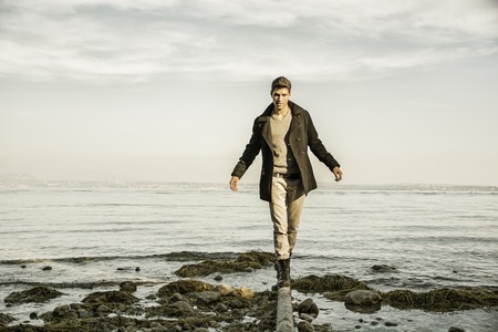 Handsome young man on a lake's shore at dusk of a sunny, peaceful day, standing