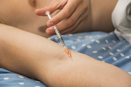Close-Up of Man Giving Self Injection with Needle Syringe While Lying in Bed - Waist Up of Bare Chested Man Injecting Arm with Drugs While Lying in Bedの写真素材