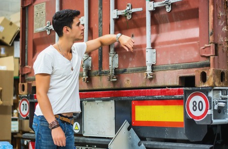 Waist Up Portrait of Young Smiling Man Next to Freight Truck - Unloading Cargo from Containerの写真素材