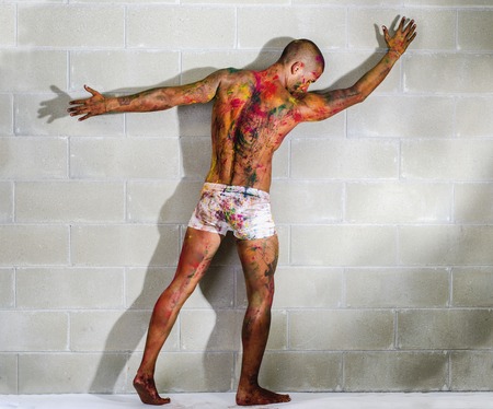 Handsome young man with skin painted all over with bright Holi colors, in front of concrete bricks wallの写真素材