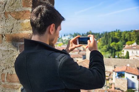 Handsome young man on a lake in a sunny, peaceful day, taking photo with cell phone of the landscapeの写真素材
