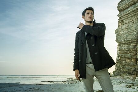 Handsome young man on a lake's shore at dusk of a sunny, peaceful day, standing