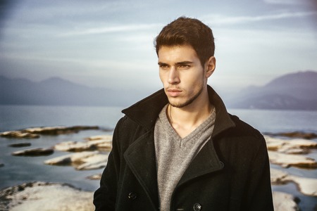 Handsome young man on a lake's shore at dusk of a sunny, peaceful day, standingの写真素材
