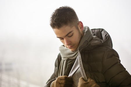 Profile view of handsome young man outdoor in winter wearing scarf, looking away thinkingの写真素材
