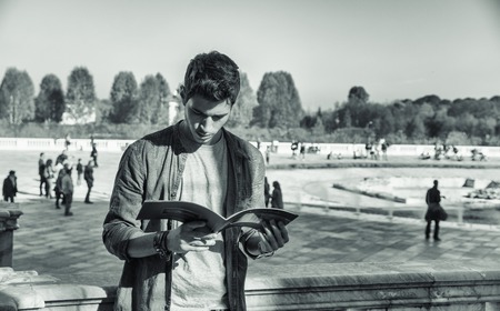 Half Body Shot of a Thoughtful Handsome Young Man, a Tourist, Holding a Guide, Looking Away Outside Historic Building in European Cityの写真素材