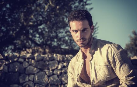 Ruggedly Handsome Man Among Trees with Shirt Unbuttoned Relaxing in Warm Sunlightの写真素材