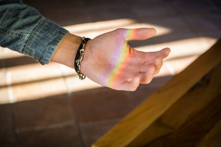 Young man showing rainbow reflection on his handの写真素材