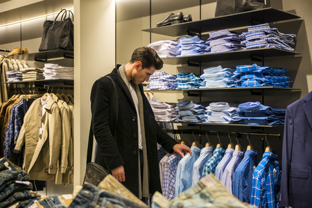 Side view of young male customer choosing shirt in menswear shopの写真素材