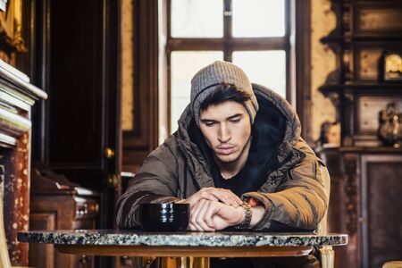 Upset black haired man sitting at table indoors and looking down.の写真素材