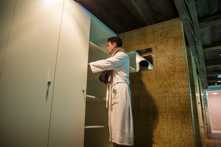 Handsome young man wearing white bathrobe, standing in spa bath next to closetの写真素材