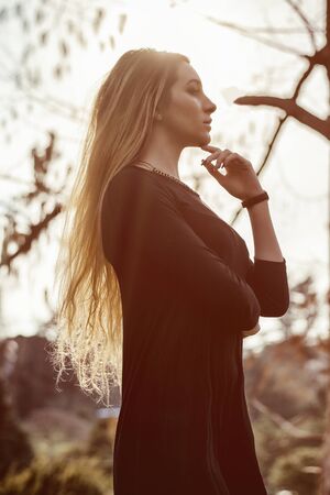 Pretty blonde young woman outdoor in city park, wearing short black dressの写真素材