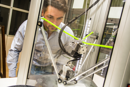 Brunet adult man working with 3D printer, observing the machine at work