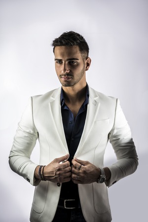 Handsome young man in blue shirt and white jacket posing on white background in studio