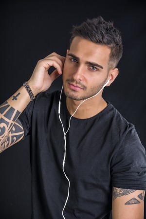 Attractive young man with earphones listening to music, on dark backgroundの写真素材