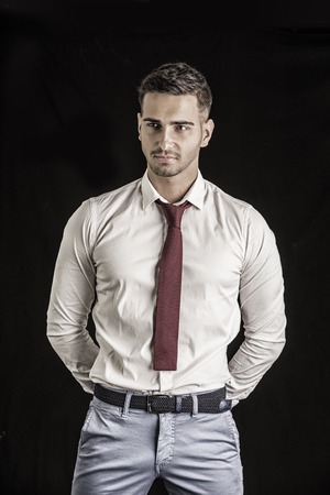 Handsome young man in in white shirt and red neck tie posing on dark background in studioの写真素材