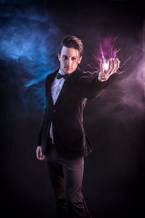 Portrait of young handsome magician in elegant suit and bow-tie holding lightning in handの写真素材